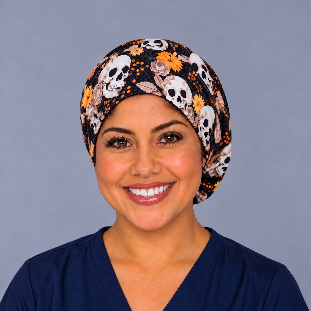 Smiling nurse in navy scrubs wearing a fall skull euro scrub cap, front view with ivory skulls and orange blooms framing the forehead