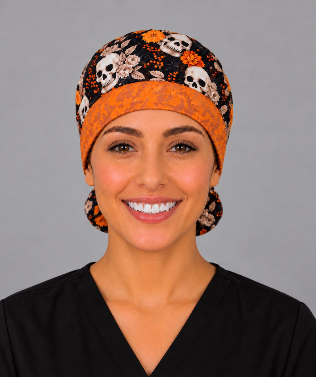 Smiling nurse in black scrubs wearing a fall skull ponytail scrub cap, front view of the textured orange hexagon band framing her forehead