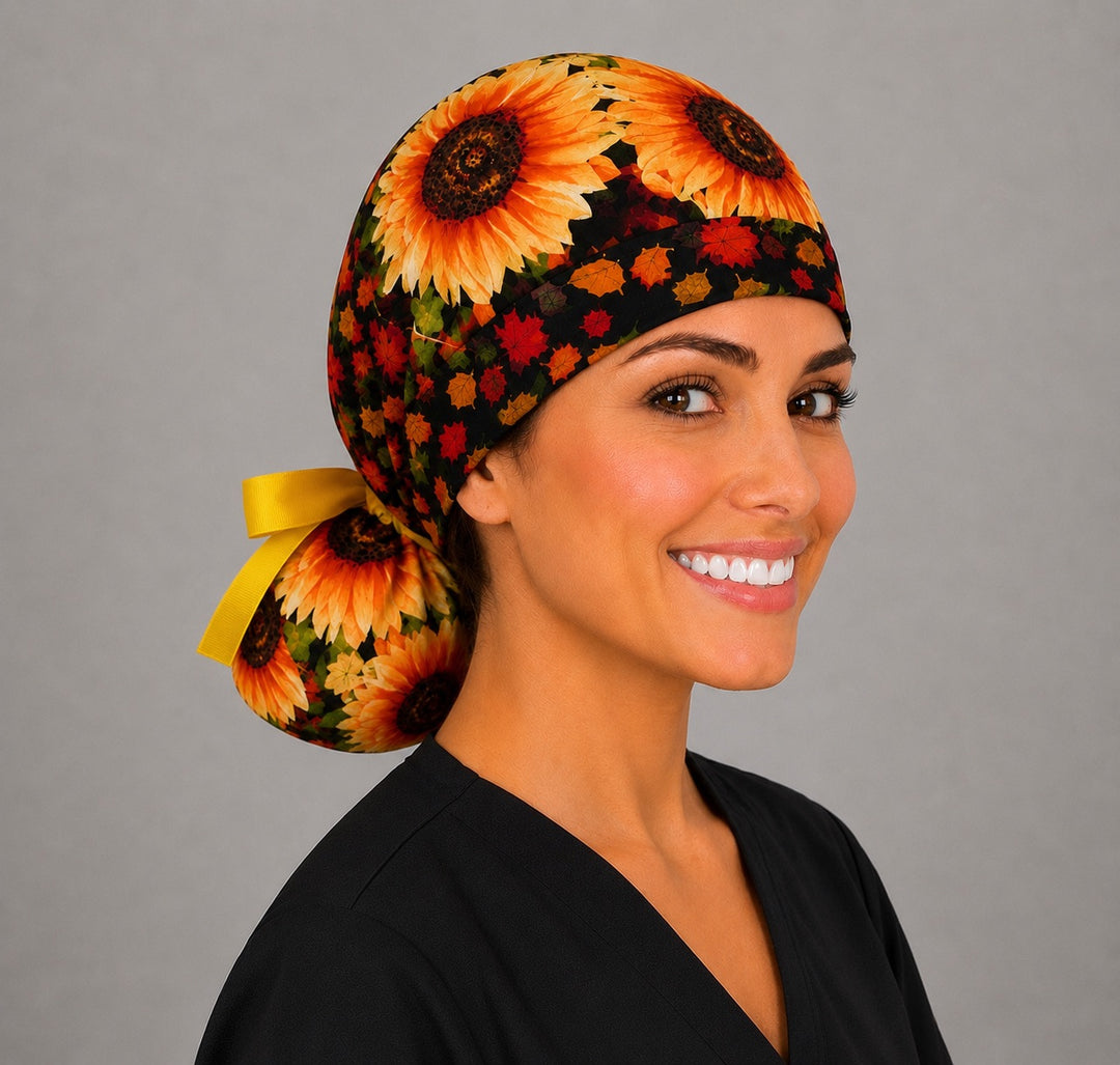 Woman wearing fall sunflower ponytail scrub cap, front view smiling with golden sunflowers and autumn leaf band with yellow ribbon tie