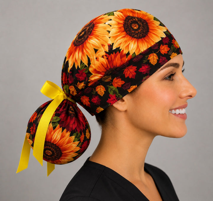 Fall sunflower ponytail surgical cap left three-quarter angle on smiling model showing golden sunflowers and colorful autumn leaves with yellow ribbon bow
