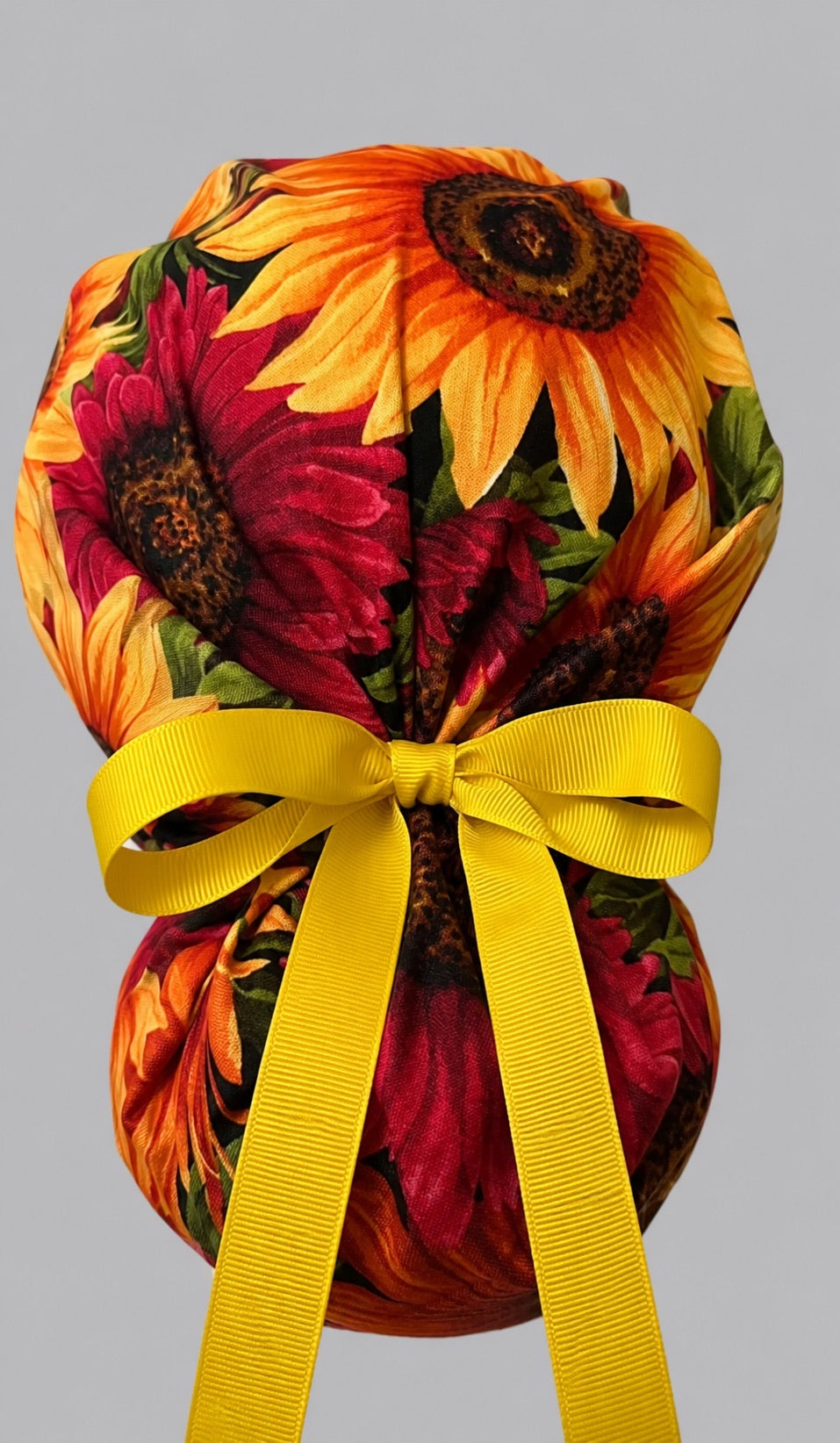 Fall sunflower ponytail nurse cap right three-quarter angle on smiling model showing golden and orange sunflowers with autumn leaf band and yellow ribbon bow