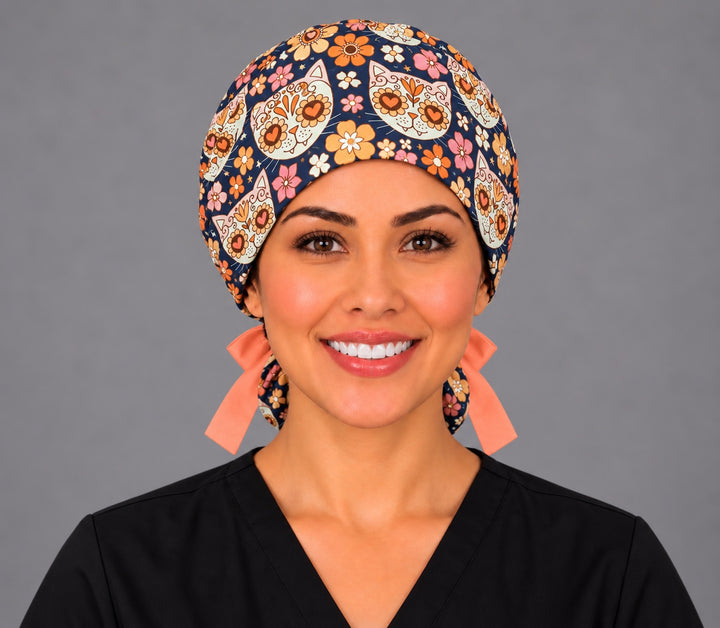 Front view of a nurse in the Fiesta Gato sugar skull cat ponytail scrub cap, heart-eyed calavera kitties on navy with peach ribbon ties
