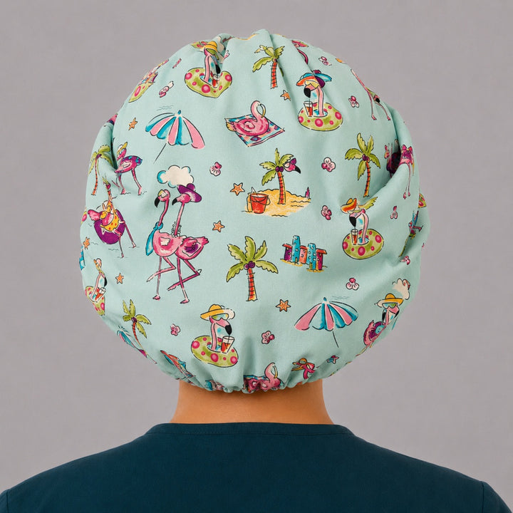 Back view of the flamingo beach bouffant scrub cap — full roomy fit with flamingos, palm trees, beach umbrellas and sandcastles on aqua