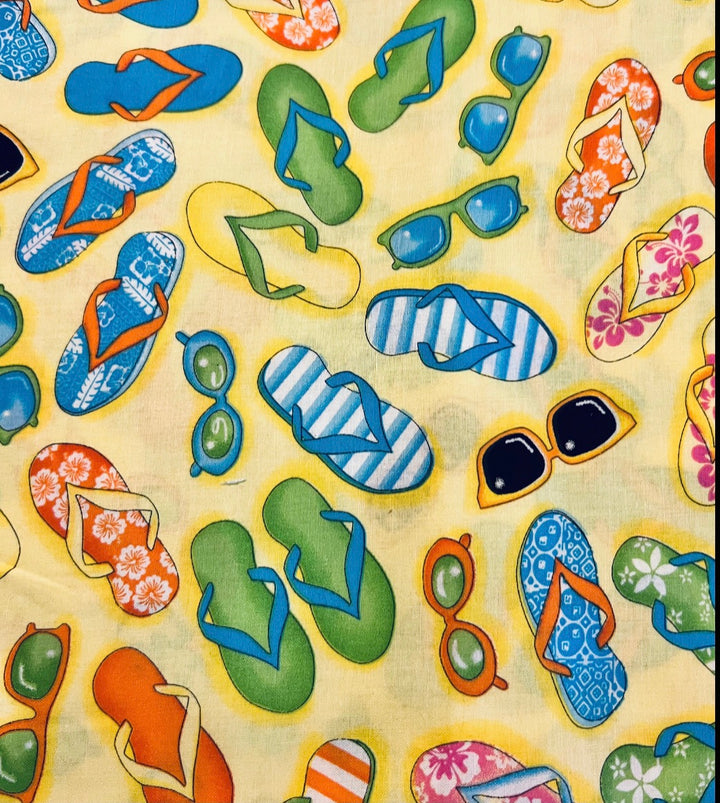 Fabric detail of the Flip Flops scrub cap — close-up of colorful flip flops and sunglasses on yellow cotton