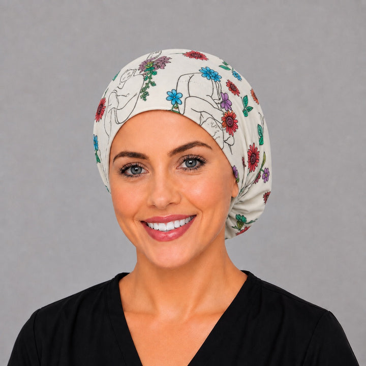 Woman wearing a floral baby Euro scrub cap, front view — newborn line art among watercolor blooms, adjustable L&amp;D surgical hat