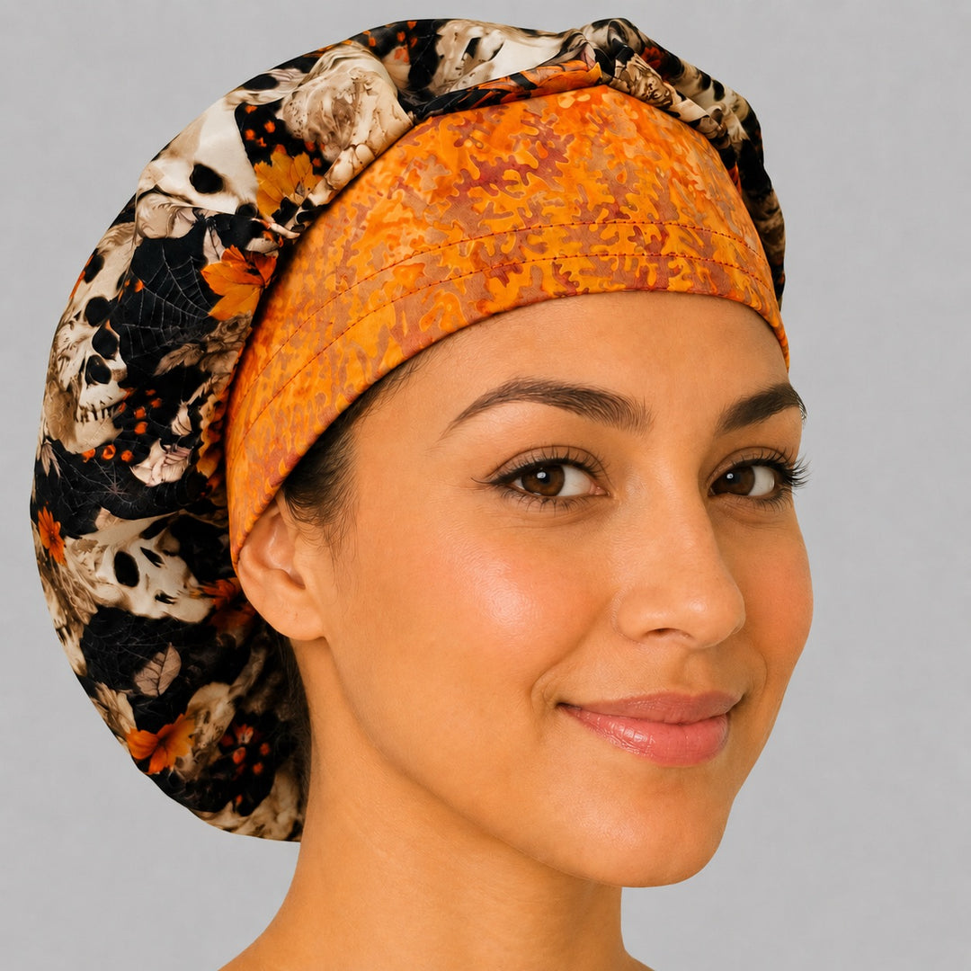 Angled view of the floral skull bouffant surgical hat — skulls, maple leaves and spiderwebs with orange batik contrast band, roomy cotton cap