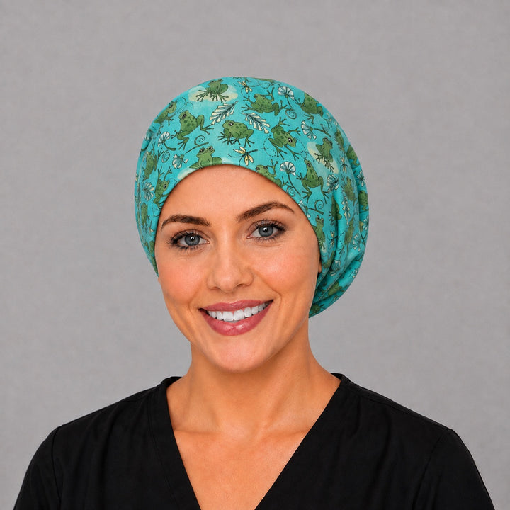 Woman wearing a frog Euro scrub cap, front view — green tree frogs and dragonflies on teal, adjustable women&