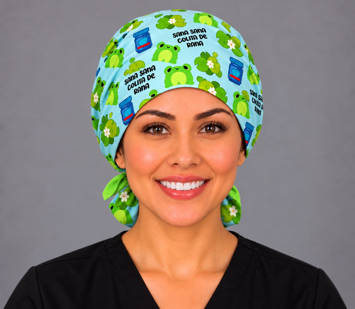 Front view of a frog ponytail surgical hat for long hair with Sana Sana lettering on sky blue