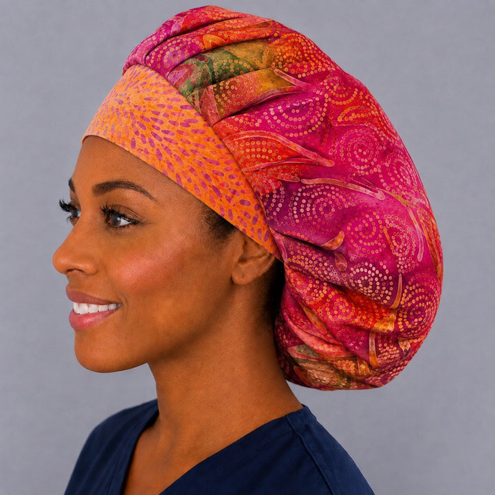 Left side profile of the fuchsia batik bouffant surgical hat — orange contrast band with swirled dot print, roomy breathable cotton cap for nurses