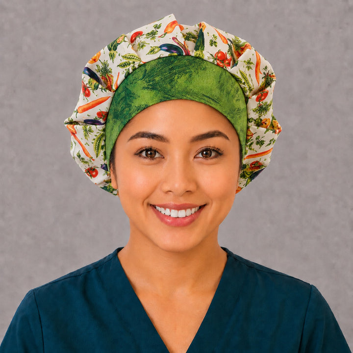 Woman wearing a garden vegetable bouffant scrub cap, front view — watercolor tomatoes, peppers and eggplants on cream with a green batik band, adjustable women&
