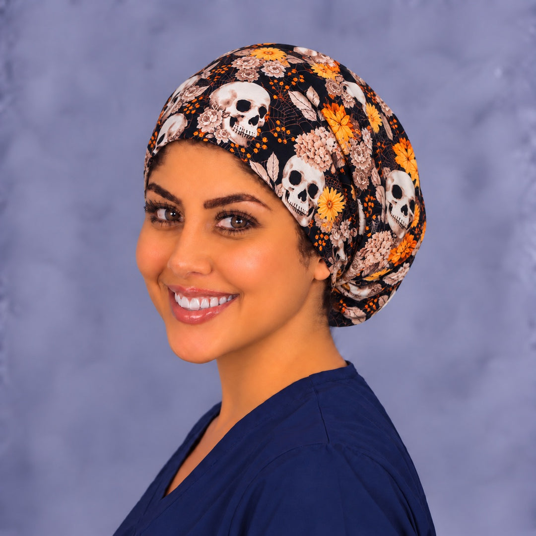 Three-quarter angle of a smiling healthcare worker in a gothic floral skull scrub hat, with dusty-rose flowers and skulls shown at true print scale