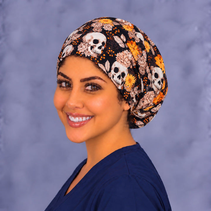 Three-quarter angle of a smiling healthcare worker in a gothic floral skull scrub hat, with dusty-rose flowers and skulls shown at true print scale