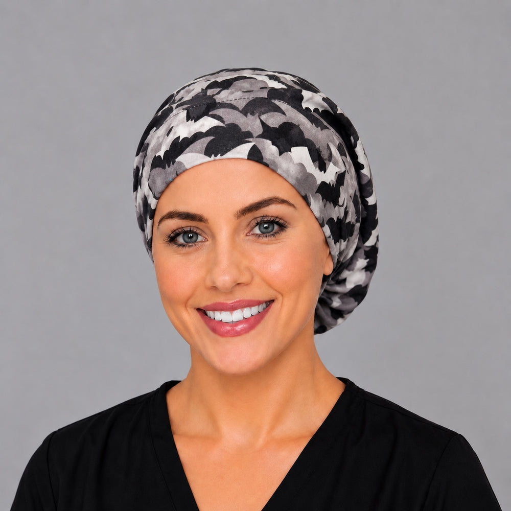 Woman wearing a Halloween bat Euro scrub cap, front view — black and grey bats in flight, adjustable surgical hat for nurses