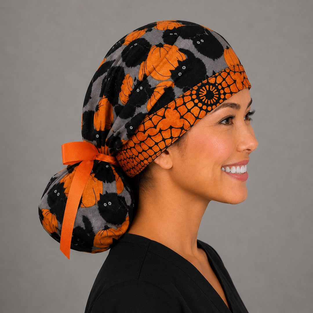 Halloween black cat and pumpkin ponytail scrub cap left side profile with full ponytail pouch of black cats and orange pumpkins and long orange ribbon ties