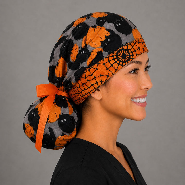 Halloween black cat and pumpkin ponytail scrub cap left side profile with full ponytail pouch of black cats and orange pumpkins and long orange ribbon ties