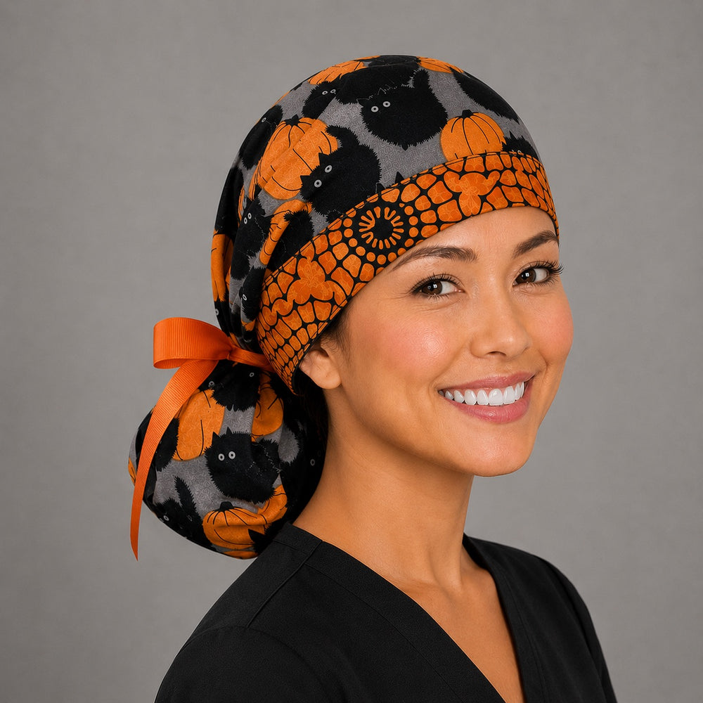 Halloween black cat and pumpkin ponytail nurse cap left three-quarter angle on smiling model showing black cats, orange pumpkins and pumpkin band with orange ribbon bow