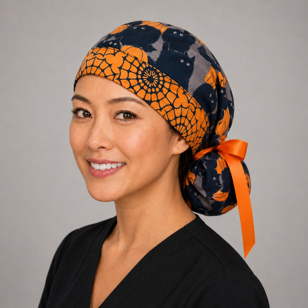 Halloween black cat and pumpkin ponytail surgical cap right three-quarter angle showing black cats and orange pumpkins on gray with orange band and orange ribbon bow