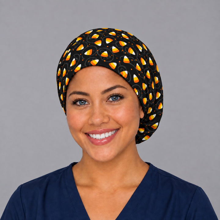 Woman wearing a Halloween candy corn Euro scrub cap, front view — orange and white candy corn on black, adjustable surgical hat