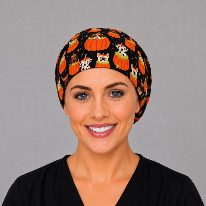 Woman wearing a Halloween dog Euro scrub cap, front view — puppies in carved pumpkins on black, adjustable surgical hat for nurses