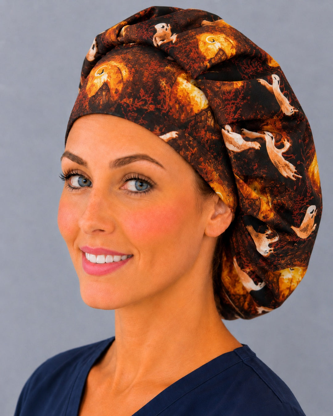 Woman wearing a Halloween ghost bouffant scrub cap, front view — ghosts and glowing jack-o'-lanterns on black, adjustable women's surgical hat