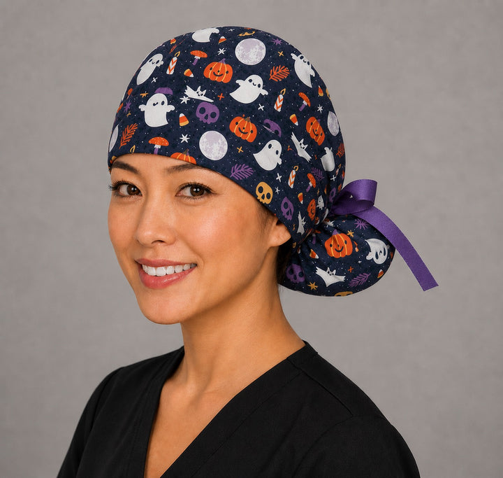 Cute ghost and pumpkin Halloween ponytail scrub cap left side profile showing gathered ponytail pouch of ghosts, pumpkins and skulls on navy with purple ribbon tie