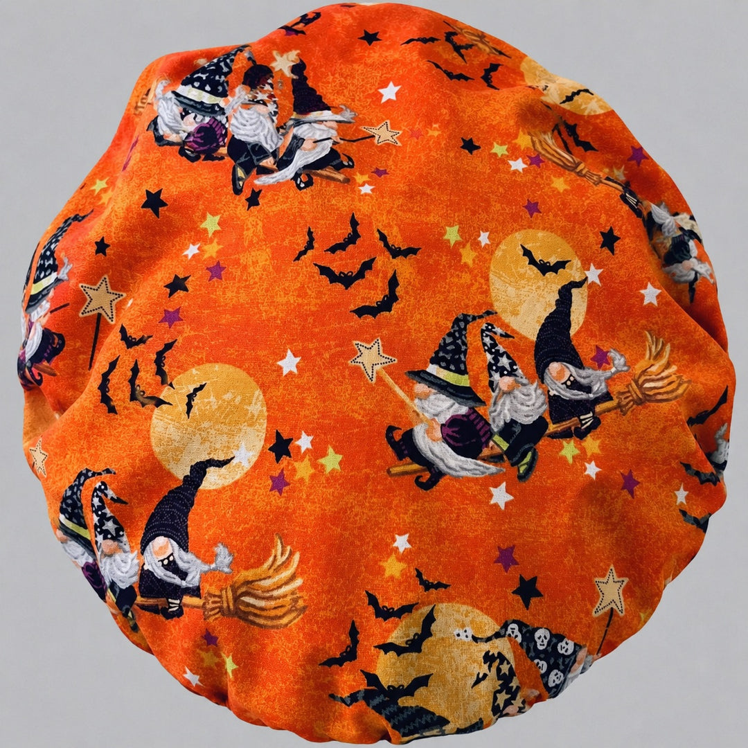 Woman wearing a Halloween gnome bouffant scrub cap, front view — orange witch gnome and bat print with lime green vine band, adjustable unisex surgical hat