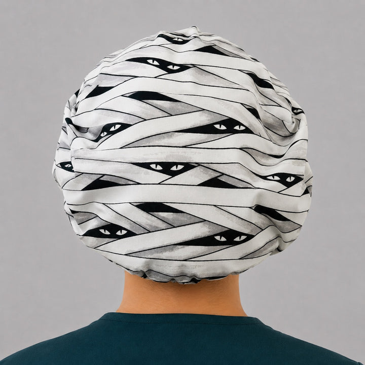 Halloween mummy bouffant scrub cap back view showing full mummy-wrap bandage print with peeking eyes on white and gray, OR World surgical hat