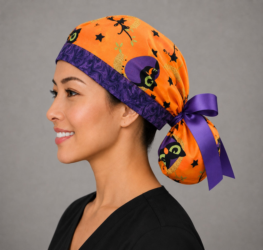 Halloween owl ponytail scrub cap back view close-up showing gathered pouch full of purple witch owls, gold moons and black stars on orange with purple grosgrain ribbon bow