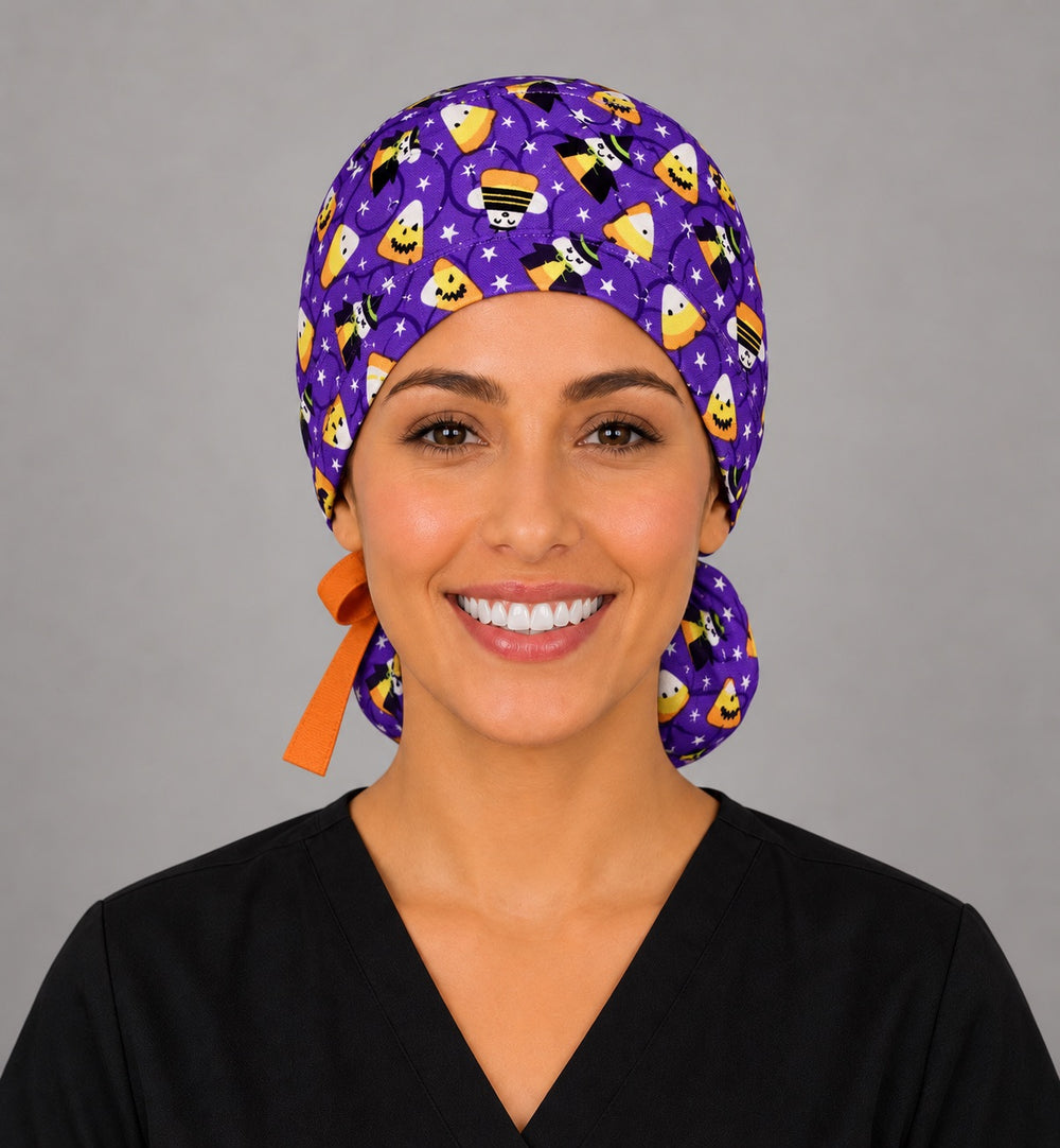 Woman wearing a candy corn witches ponytail scrub cap, front view — smiling candy corn and witches on purple with orange bow