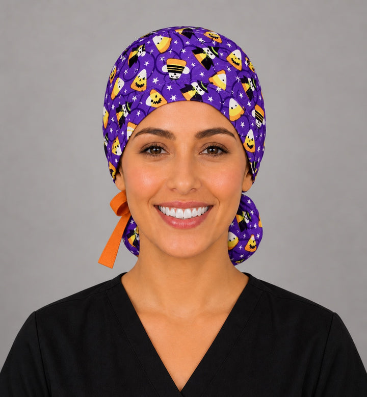 Woman wearing a candy corn witches ponytail scrub cap, front view — smiling candy corn and witches on purple with orange bow