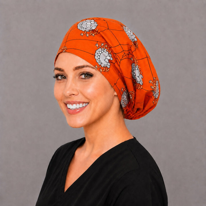 Woman wearing a Halloween spider Euro scrub cap, front view — googly-eyed monster spiders on orange with black webs, adjustable surgical hat