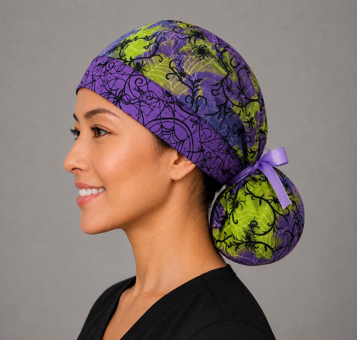 Halloween spider ponytail surgical cap left three-quarter angle on smiling model showing black spiders and webs on purple and lime green with purple ribbon bow