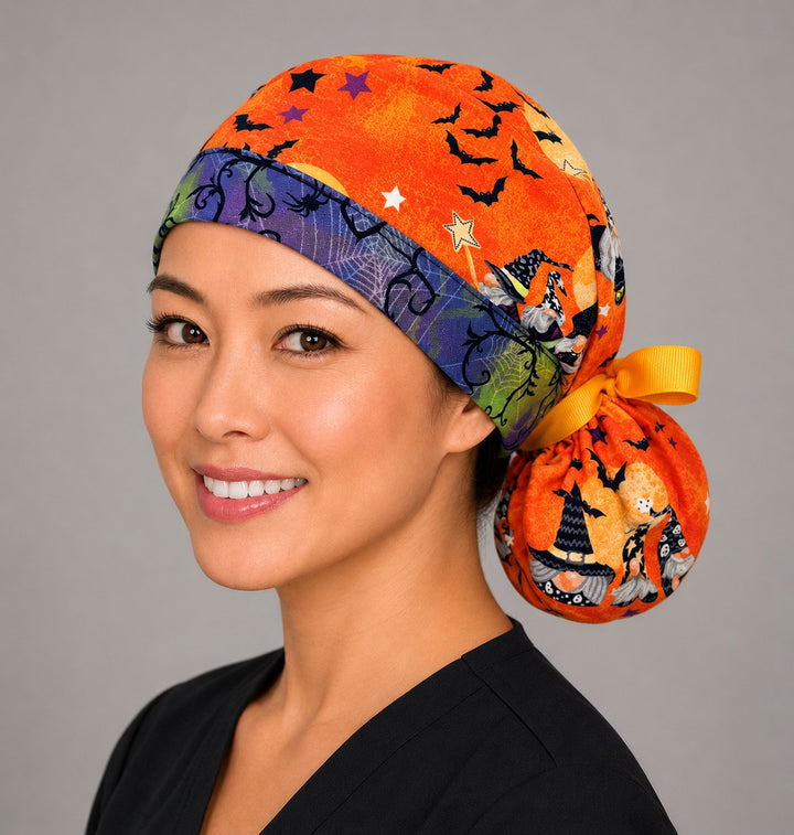 Halloween witch gnome ponytail nurse cap right three-quarter angle on smiling model showing witch gnomes, bats and stars on orange with spiderweb band and yellow ribbon bow