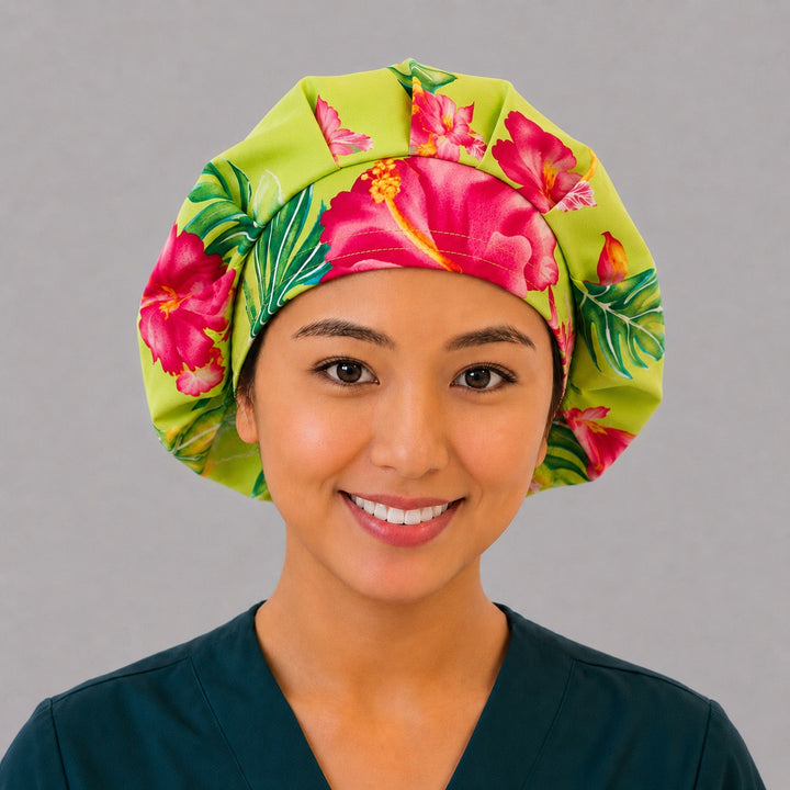 Hawaiian hibiscus bouffant scrub cap left three-quarter angle on smiling model showing pink and orange hibiscus and monstera on lime green, women&