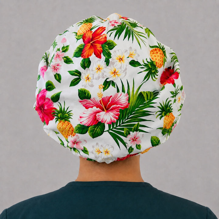 Back view of the Hawaiian pineapple bouffant scrub cap — full gathered fit showing hibiscus, plumeria and palm leaves across the white crown