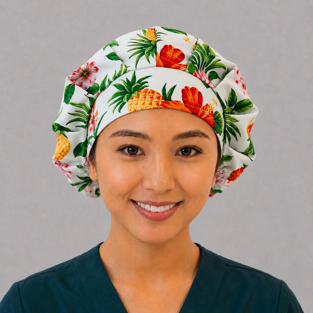 Woman wearing a Hawaiian pineapple hibiscus bouffant scrub cap, front view — tropical hibiscus, plumeria and pineapples on white, adjustable women's surgical hat