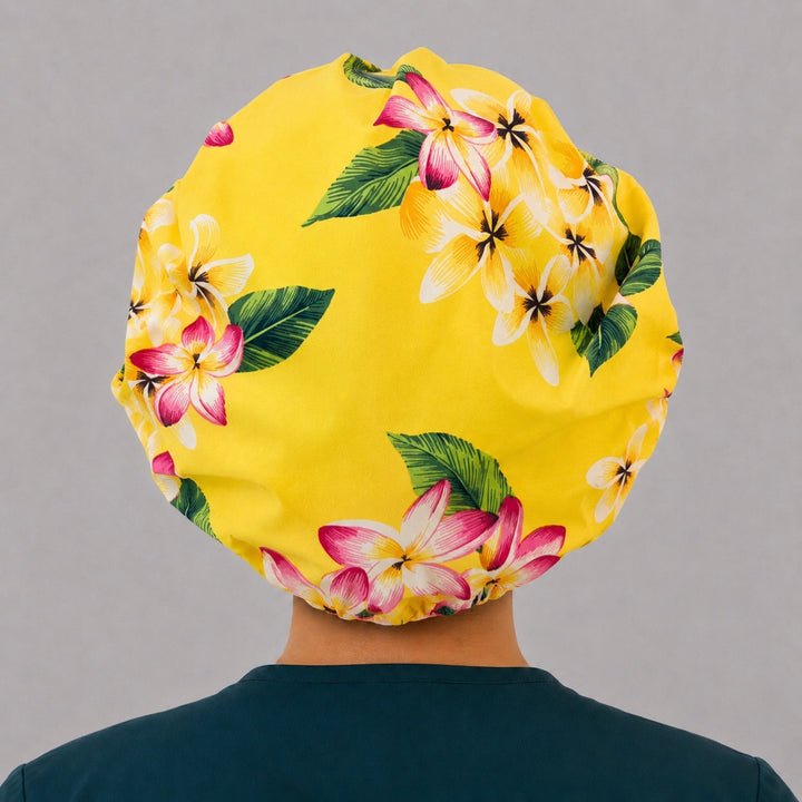 Hawaiian tropical floral bouffant scrub cap for women, front view, yellow and pink plumeria print with pink swirl band, handmade surgical hat by OR World