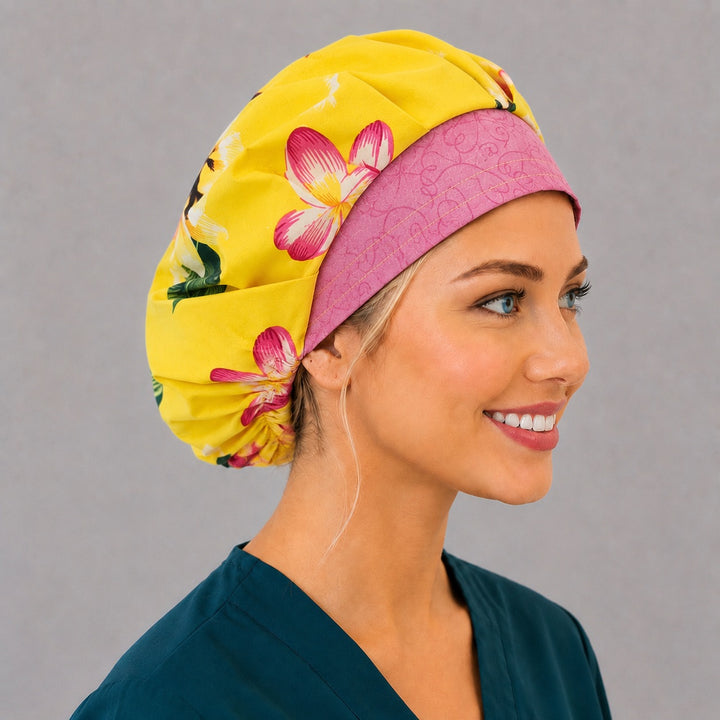 Hawaiian tropical floral bouffant scrub cap left three-quarter angle on smiling model showing yellow and pink plumeria with pink swirl band, OR World tropical nurse hat