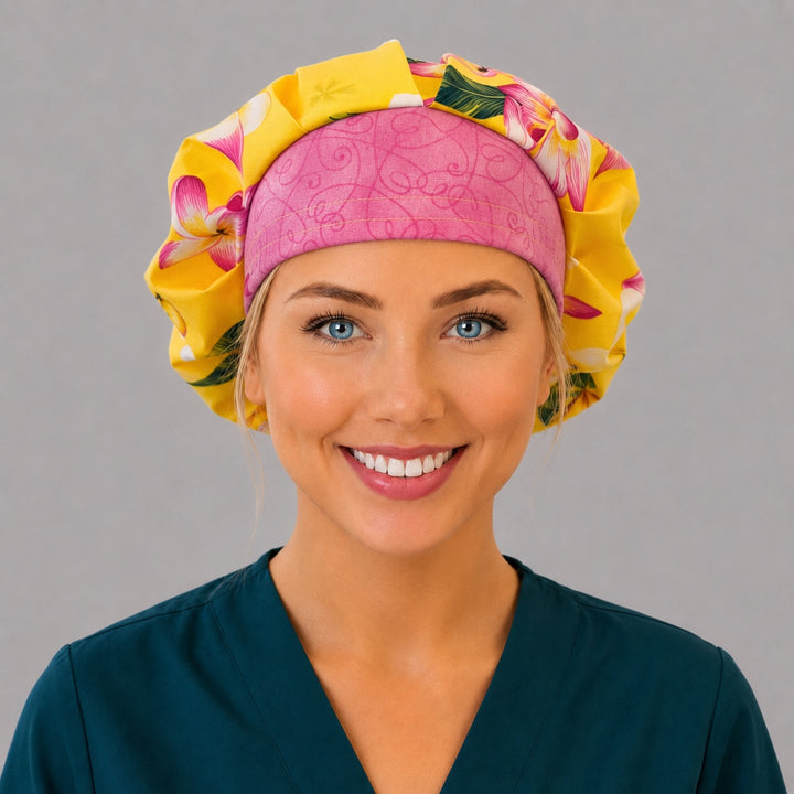 Hawaiian tropical floral bouffant scrub cap right three-quarter angle on smiling model showing yellow pink plumeria and pink swirl band, women&