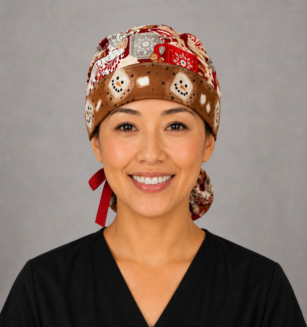 Woman wearing hot chocolate ponytail scrub cap, front view smiling with cocoa mugs, gingerbread and marshmallows on red with snowman band and red ribbon tie