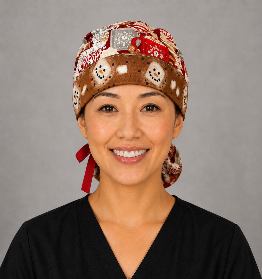 Woman wearing hot chocolate ponytail scrub cap, front view smiling with cocoa mugs, gingerbread and marshmallows on red with snowman band and red ribbon tie