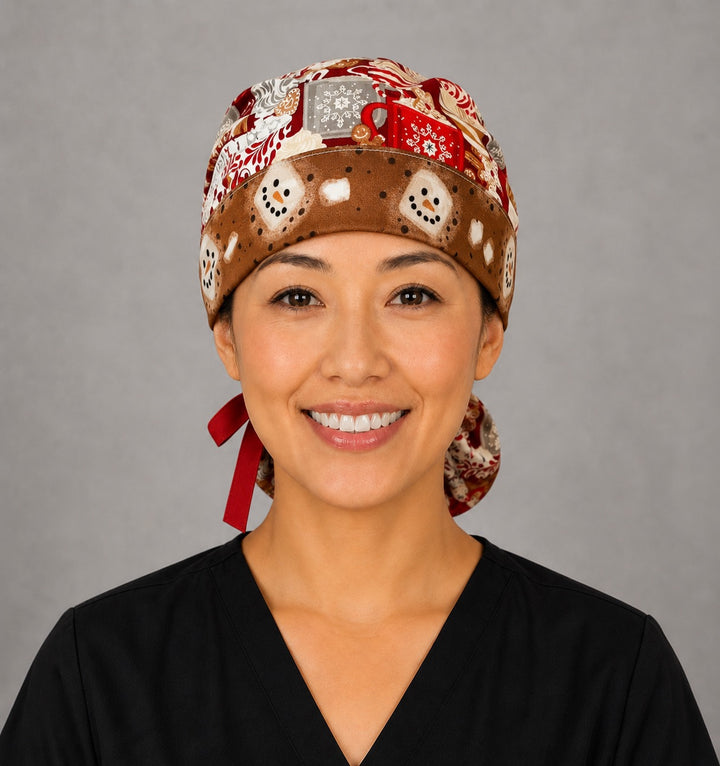 Woman wearing hot chocolate ponytail scrub cap, front view smiling with cocoa mugs, gingerbread and marshmallows on red with snowman band and red ribbon tie