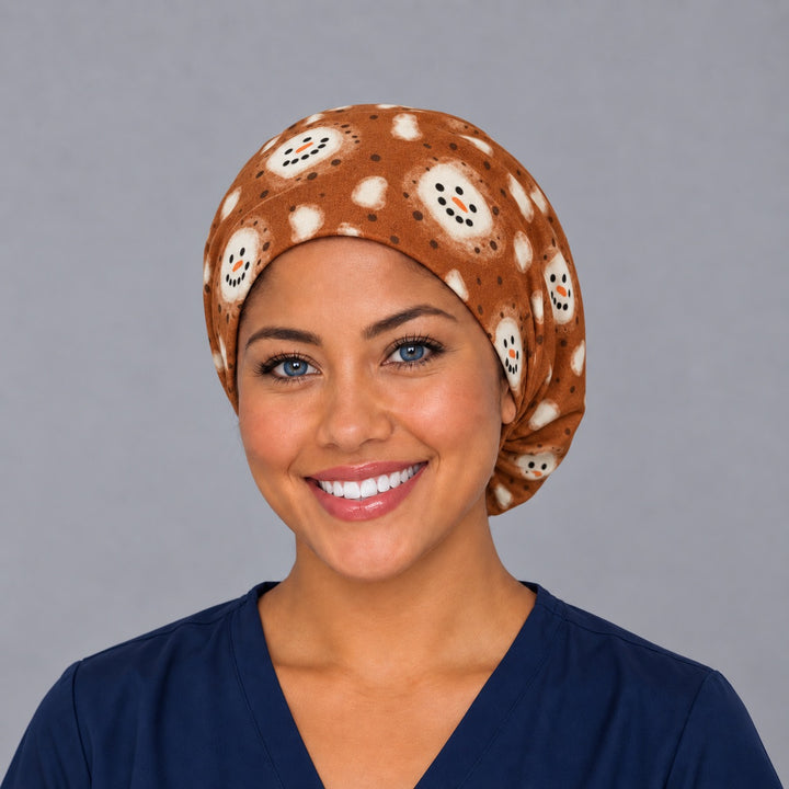 Woman wearing a hot cocoa marshmallow Euro scrub cap, front view — snowman-face marshmallows on cinnamon brown, adjustable winter surgical hat