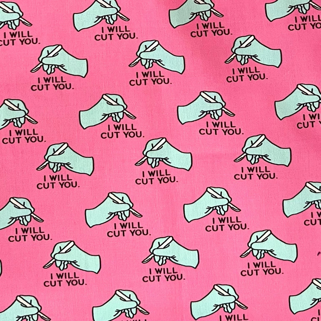 Close up of I Will Cut You fabric on hot pink cotton, gloved hand and scalpel print detail of the funny surgery tie back scrub cap