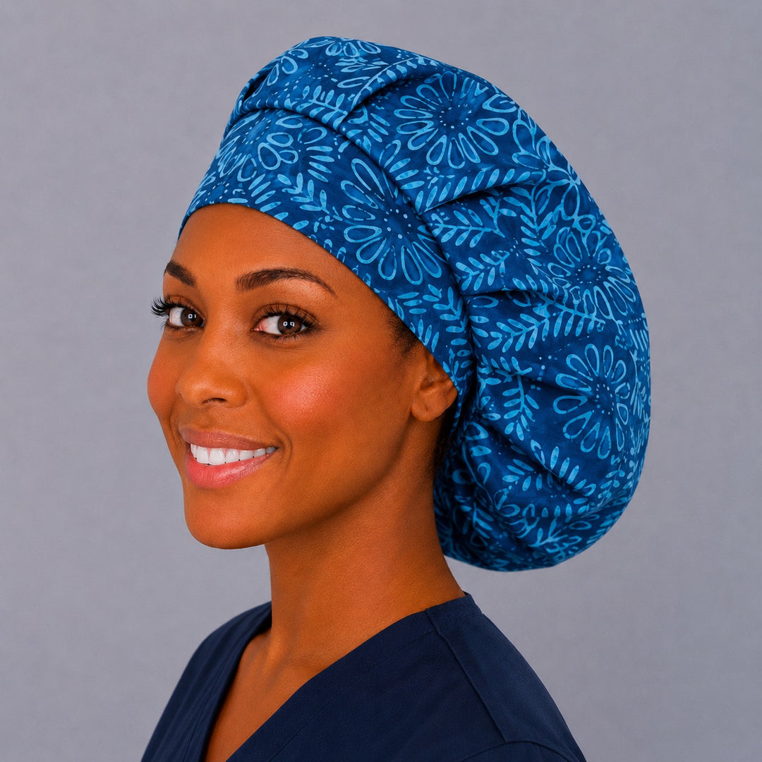 Woman wearing an indigo blue batik floral bouffant scrub cap — outlined flowers and vines in midnight and neon blue, adjustable women's surgical hat
