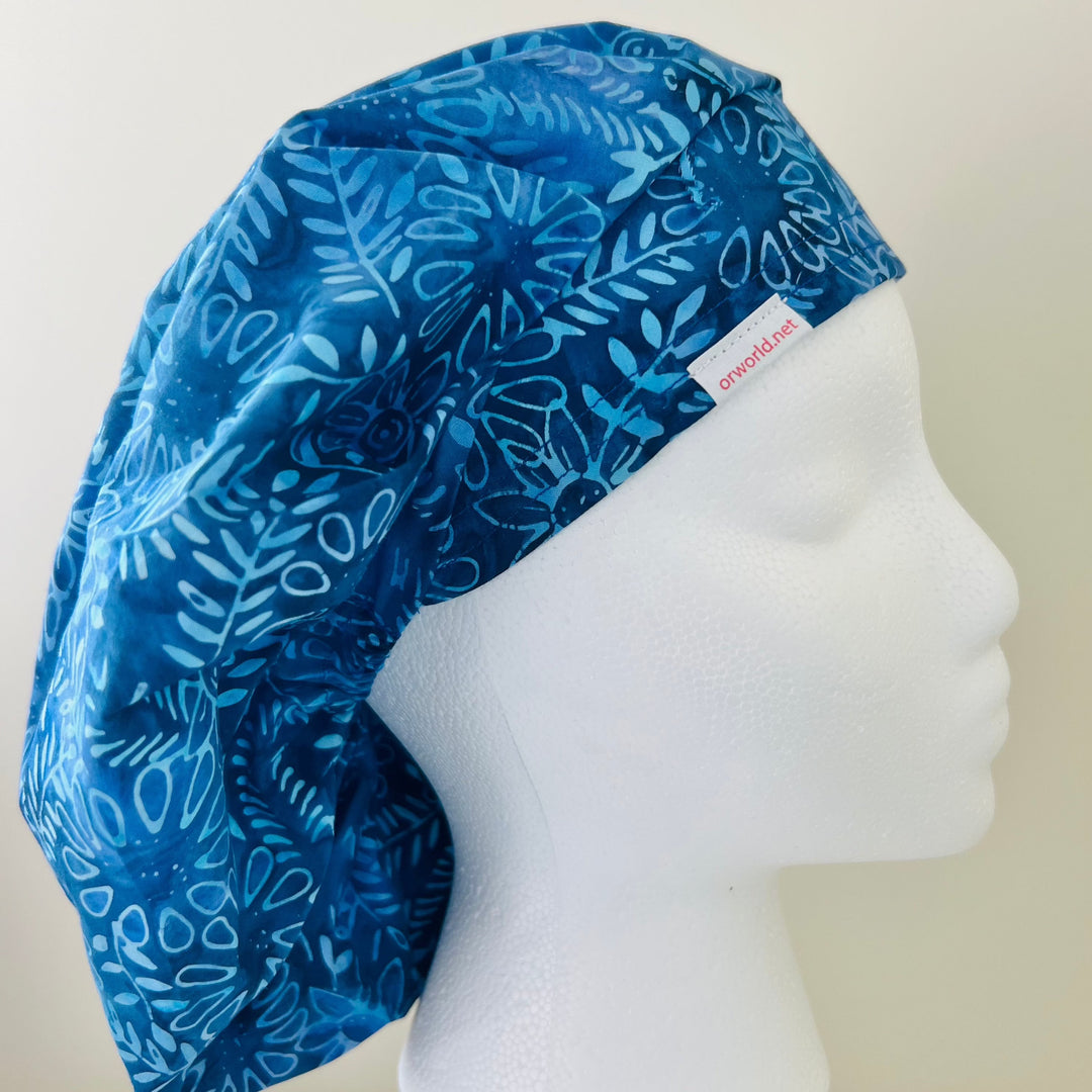 Indigo blue batik floral bouffant scrub cap with light-blue outlined flowers on a model — handmade-in-USA surgical hat for women from OR World.