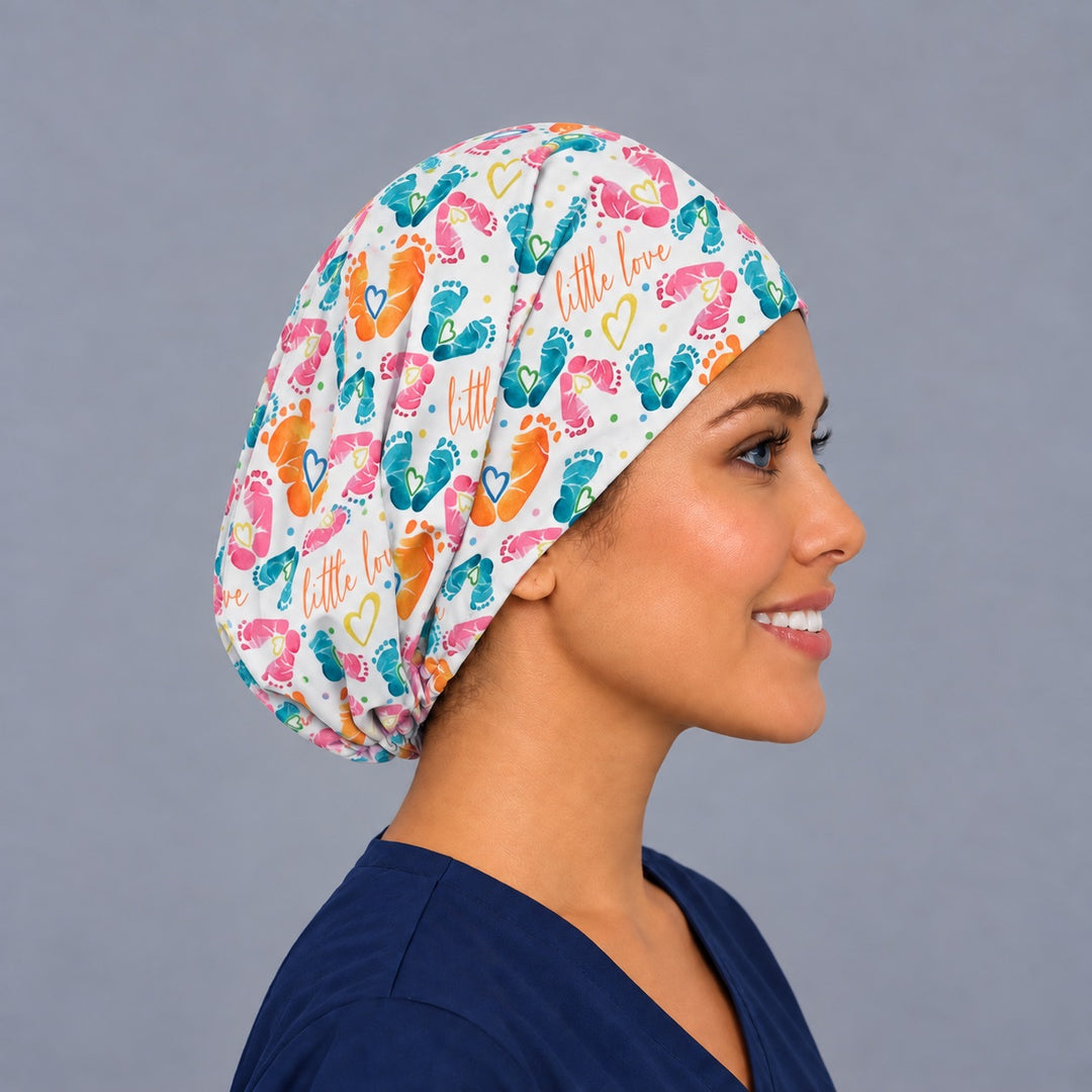 Right side profile of an L&amp;D nurse footprint surgical cap, with teal and pink watercolor baby feet along the side and the elastic gathered behind the ear