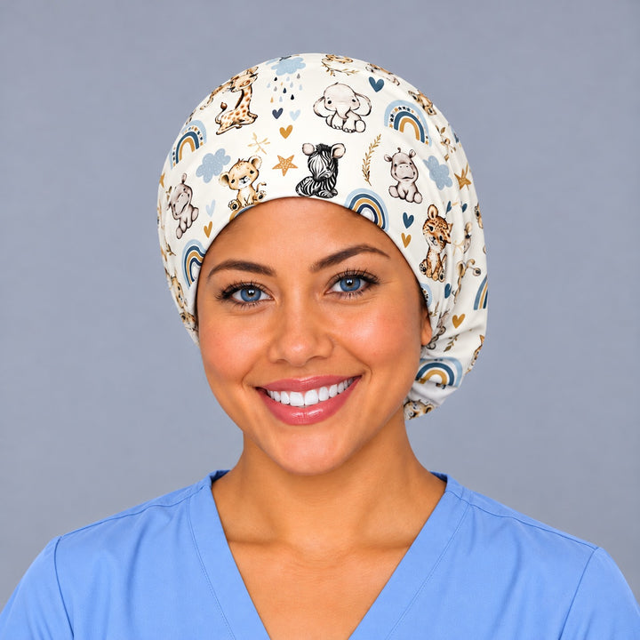 Smiling nurse in ceil blue scrubs wearing a labor and delivery euro scrub cap, front view of baby safari animals and boho rainbows on cream across the forehead