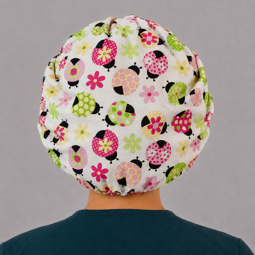 Woman wearing a ladybug bouffant scrub cap, front view — pink and green polka-dot ladybugs with a pink daisy band, adjustable women&