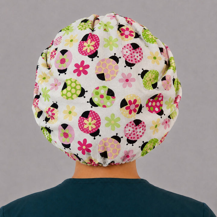 Woman wearing a ladybug bouffant scrub cap, front view — pink and green polka-dot ladybugs with a pink daisy band, adjustable women&